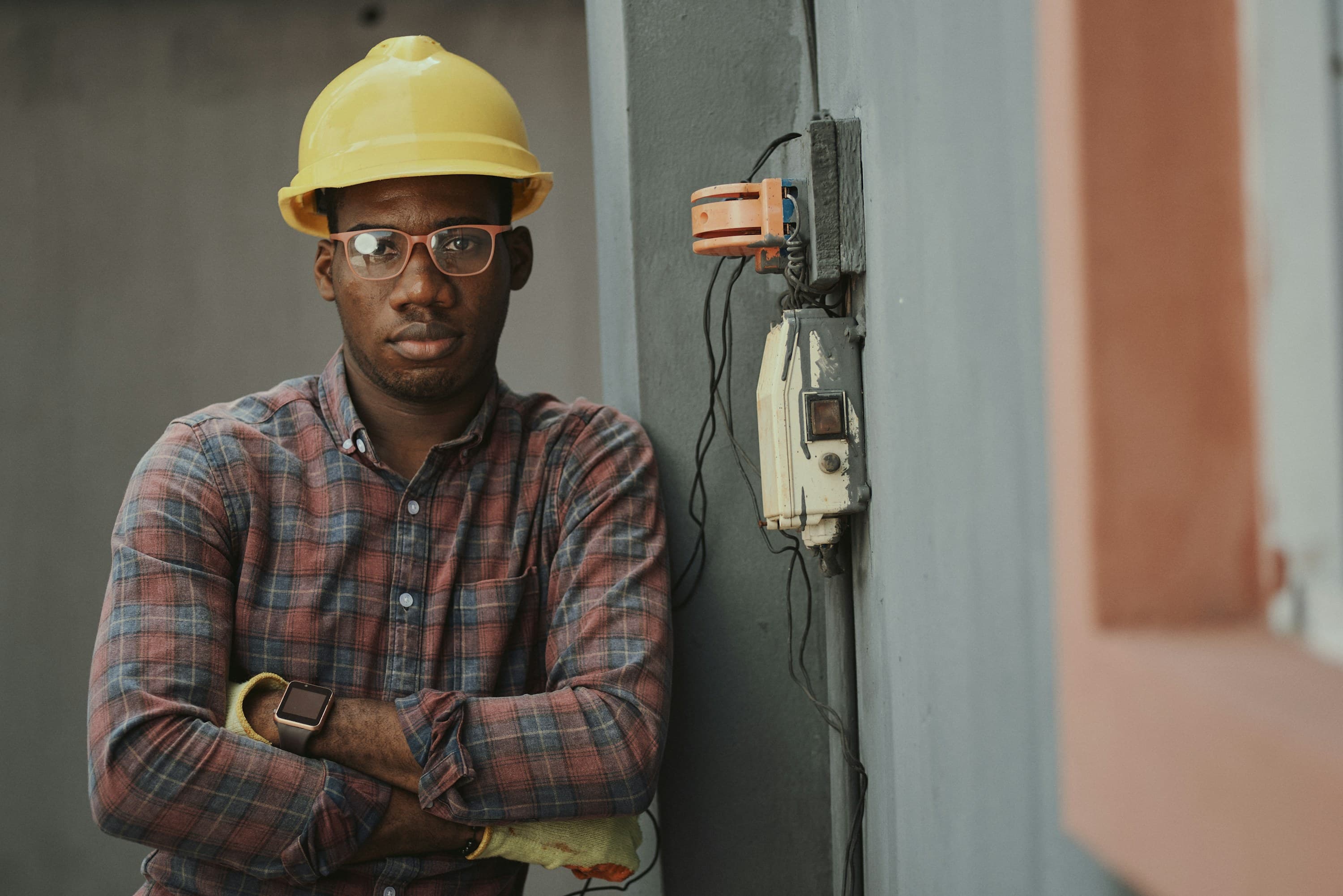 Confident engineer in a hard hat standing beside electrical wiring at an industrial site